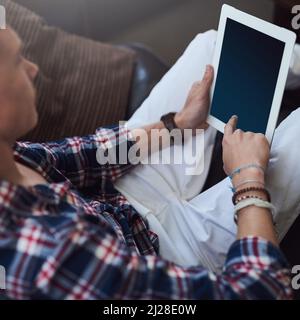 Controllare i feed dei social media. Scatto ad angolo alto di un giovane uomo che usa il tablet mentre si siede sul divano a casa. Foto Stock