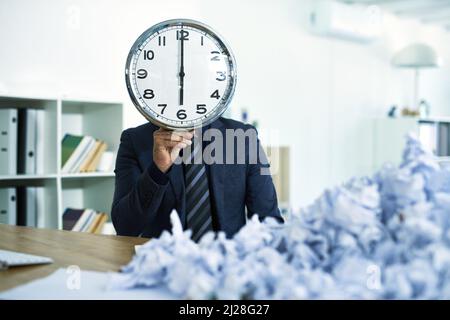 Tempo di uscita del whens. Colpo di un uomo d'affari seduto alla sua scrivania sopraffatto da documenti che tengono un orologio di fronte al suo volto. Foto Stock