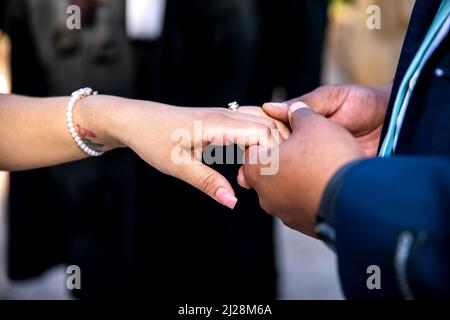 Indossare l'anello di messa sul dito della sposa primo piano di mani e anello Foto Stock