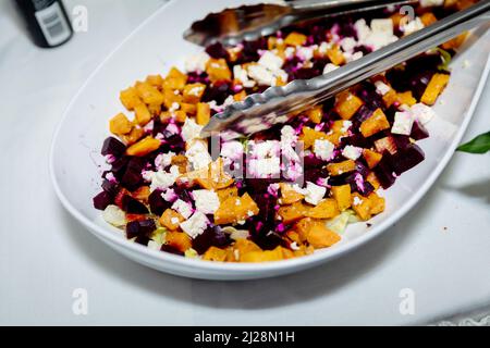 Zucca arrosto vegetariana, barbabietola e insalata di feta in un server bianco su una tovaglia bianca Foto Stock