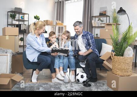 Benvenuti a casa. Due bambini carini, ragazzo e ragazza, aiutando i loro genitori a disimballare le scatole durante il trasferimento. Giovane famiglia felice sentirsi eccitato circa il trasferimento alla nuova casa. Foto Stock