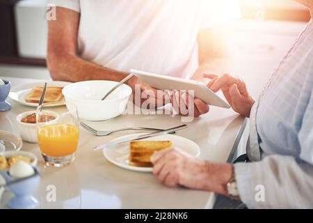 Navigazione a colazione. Primo piano di una coppia anziana utilizzando un tablet digitale mentre si consuma la colazione a casa. Foto Stock