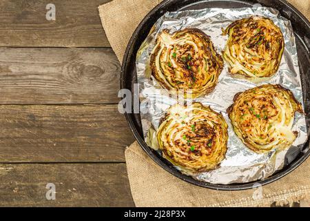 Bistecche di cavolo vegano fatte in casa con erbe e spezie. Cibo sano pronto a mangiare su una teglia da forno. Vecchio sfondo in legno, vista dall'alto Foto Stock