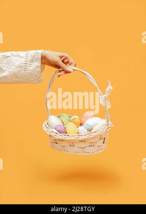 Un'idea di Pasqua creativa e colorata. Composizione di un cesto bianco e uova colorate decorate con foglie d'oro. La mano di una donna tiene un cesto con un pizzo Foto Stock