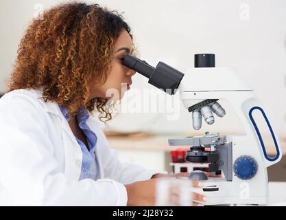 Uno sguardo più da vicino. Scatto corto di una giovane scienziata femminile che guarda al microscopio. Foto Stock