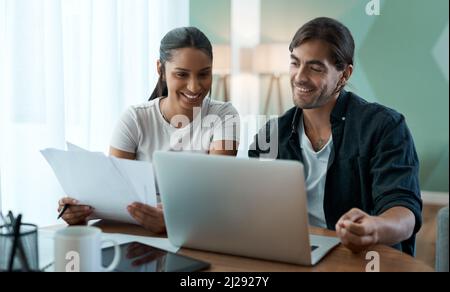 Facciamo un buon team. Scatto di una giovane coppia che fa la documentazione mentre usa un laptop a casa. Foto Stock