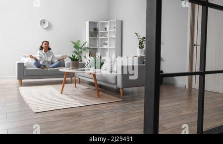 Ragazza adolescente afroamericana meditando mentre si siede sul divano a casa Foto Stock