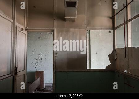 Immagine di un interno danneggiato di un edificio abbandonato con una stanza piena di polvere, rifiuti e una scrivania rimanente. Foto Stock