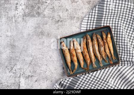 Pan il capelin fritto o il pesce odorato su una piastra rettangolare su uno sfondo grigio scuro. Vista dall'alto, disposizione piatta Foto Stock