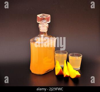 Liquore fatto in casa a base di mango e fette di frutta esotica matura su sfondo nero. Primo piano. Foto Stock