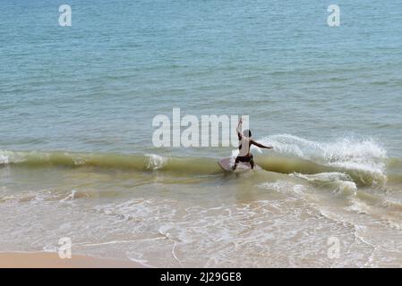 Uomo in skimming cattura un'onda in una spiaggia di Aonang, Krabi, Thailandia Foto Stock
