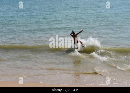 Uomo in skimming cattura un'onda in una spiaggia di Aonang, Krabi, Thailandia Foto Stock