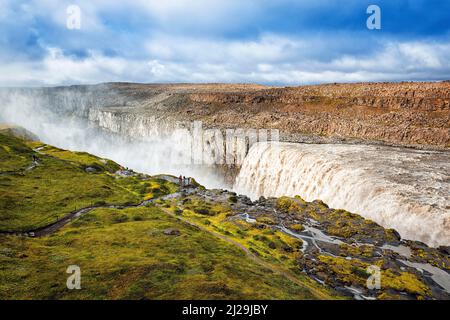 Dettifoss, turisti in una gola, cascata con le masse d'acqua in caduta, foschia, fiume Joekulsa a Fjoellum, Islanda settentrionale, Islanda Foto Stock