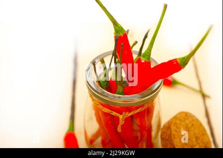 Peperoncini rossi su un vaso di vetro su un tavolo rustico in legno bianco Foto Stock