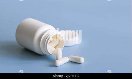 Capsule bianche sparse da un contenitore bianco di plastica per medicinali Foto Stock