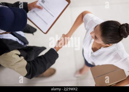 Grazie per il vostro servizio veloce ed affidabile. Colpo ad angolo alto di un uomo di consegna che agita le mani con una donna d'affari in un ufficio. Foto Stock