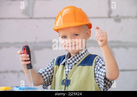 Bambino in casco protettivo arancione con strumenti per la ristrutturazione. Sorridente felice bambini costruttore e riparazione. Foto Stock