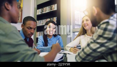 Fanno tutti i loro progetti di gruppo insieme. Scatto ritagliato di un gruppo di studenti universitari che lavorano a un progetto di gruppo in biblioteca. Foto Stock