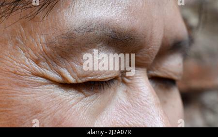 Rughe intorno ad occhio chiuso dell'anziano asiatico. Primo piano. Foto Stock