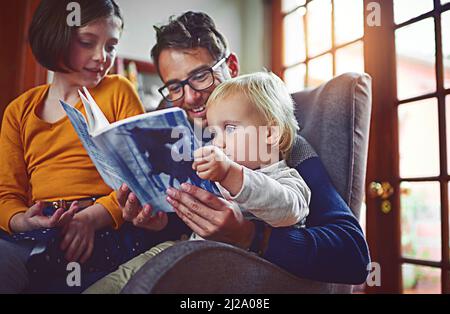 Essi godono di storia tempo come una famiglia. Shot di padre che legge un libro con suo figlio piccolo e figlia a casa. Foto Stock