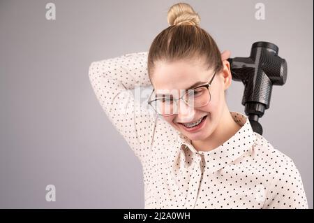 Donna sorridente con bretelle usa una pistola massaggiatore per la schiena. Foto Stock