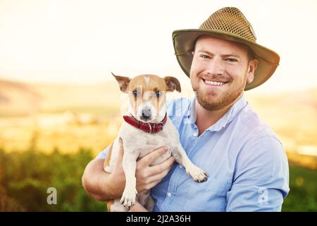 Il migliore amico di uomo può anche essere il migliore impiegato di uomo. Shot di un agricoltore felice che tiene il suo cane. Foto Stock