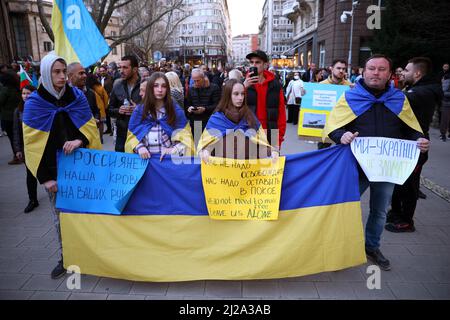 Sofia, Bulgaria - 24 marzo 2022: La gente ha segnali di protesta e la bandiera nazionale Ucraina durante una manifestazione a sostegno dell'Ucraina un mese dopo Ru Foto Stock