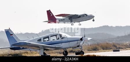 Helgoland, Germania. 25th Mar 2022. Un velivolo privato si riscalda su un grembiule del campo aereo sulla duna di Helgoland, mentre un volo di linea della Ostfriesischer Flug-Dienst (OFD) decollera sullo sfondo. Credit: Markus Scholz/dpa/Alamy Live News Foto Stock