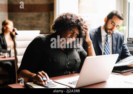 Donna d'affari con mano in capelli utilizzando il laptop da uomo d'affari che lavora in ufficio Foto Stock