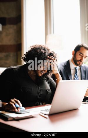 Donna d'affari preoccupata con mano in capelli usando il laptop da uomo d'affari che lavora in ufficio Foto Stock