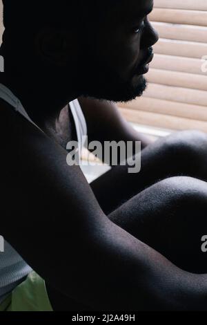 L'uomo che abbraccia le ginocchia e soffre di disturbi mentali a casa Foto Stock