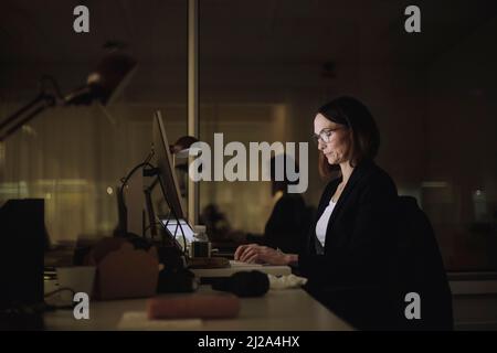 Donna d'affari che si concentra mentre lavora su un notebook in ufficio di notte Foto Stock
