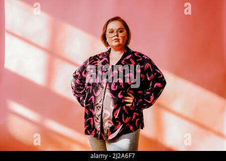 sorridente giovane donna in posa in studio con le mani sui lati rosso zenzero Foto Stock