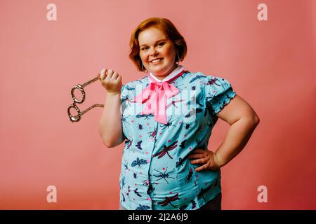 sorridente giovane donna ritratto in studio tenendo occhiali su sfondo rosa rosso zenzero Foto Stock