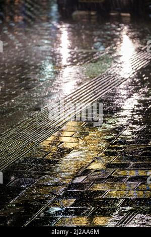 Riflessi dalle luci di natale e auto che passano su un pavimento bagnato e strada di notte. Foto Stock