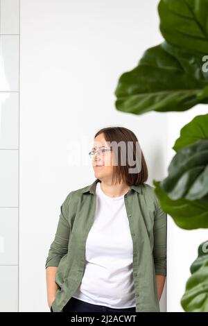 Giovane donna in piedi vicino a un muro bianco, sorridente. Foto Stock