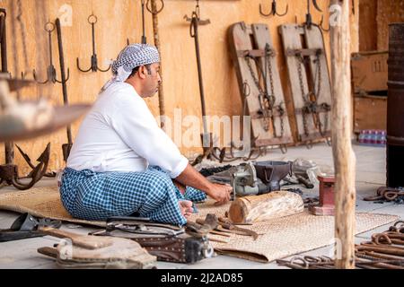 Primo piano delle mani arabe di Ironsmith che fanno artigianato di ferro battuto usando gli attrezzi tradizionali della mano con il fondo della fornace Foto Stock