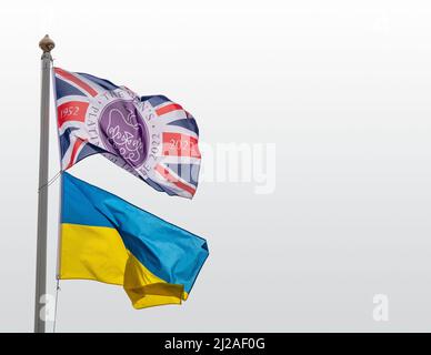 La bandiera Platinum Jubilee Union Jack vola su un palo insieme alla bandiera bicolore della Repubblica popolare Ucraina con cielo chiaro chiaro chiaro alle spalle Foto Stock