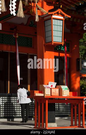 Colpo verticale di una donna che prega nel Santuario Shinto di Fushimi-Inari Taisha, Kyoto, Giappone Foto Stock