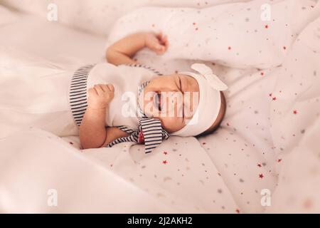 Piangendo e gesturando una bambina di dieci settimane a letto. Foto Stock