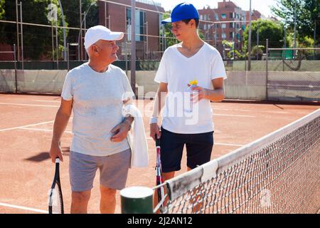 nonno e nipote parlano sul campo giocando a tennis Foto Stock