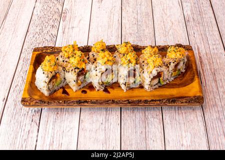 Sushi al drago Uramaki con salsa di soia, avocado, alghe nori, tonno rosso, erba cipollina su un piatto di legno, con formaggio cremoso e tavola bianca Foto Stock