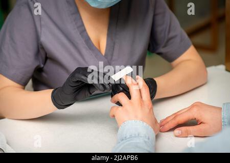 Primo piano delle mani caucasiche di un manicurista professionale stanno archiviando le unghie di una giovane donna. Giovane donna caucasica che riceve una manicure da un estetista con una lima del chiodo in un salone del chiodo Foto Stock