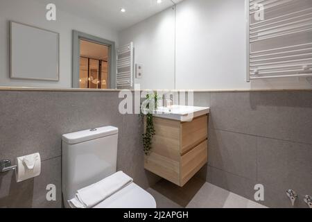 Bagno con lavabo in porcellana su armadietto in legno, specchio da parete a parete integrato, portasciugamani riscaldato bianco Foto Stock