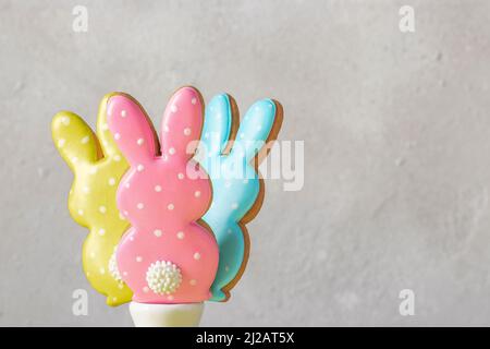 Tre Pasqua coloratissimi pani di zenzero sotto forma di conigli carini su sfondo grigio chiaro. Concetto di Pasqua. Spazio di copia Foto Stock