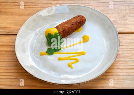 Antipasto di crocchette fritte condito con salsa di senape, antipasto mediterraneo. Su un piatto su sfondo di legno primo piano. Foto Stock