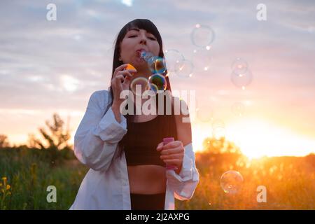 bella giovane donna che fa bolle di sapone in campo verde estate al tramonto. tempo felice pacifico. generazione millenaria. Foto Stock
