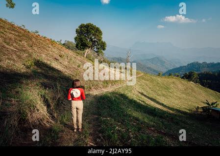 Una donna in manica lunga rossa con un cappello bianco cammina sulle praterie secche dorate di Hadubi, Chiang mai, Thailandia. Foto Stock