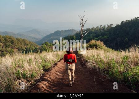 Una donna in manica lunga rossa con un cappello bianco cammina sulle praterie secche dorate di Hadubi, Chiang mai, Thailandia. Foto Stock