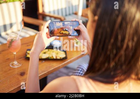 Quei giorni grassa del trucco. Foto retroguarata di una donna irriconoscibile che parla un'immagine del suo pasto in un ristorante all'aperto. Foto Stock